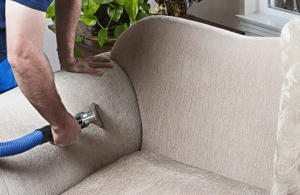 Professional upholstery cleaner deep-cleaning a fabric sofa with a handheld extraction tool and hose, Madison, WI.